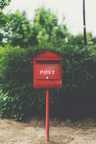 Red post mailbox surrounded by greenery — Mail by Melon quarterly party envelope subscription.