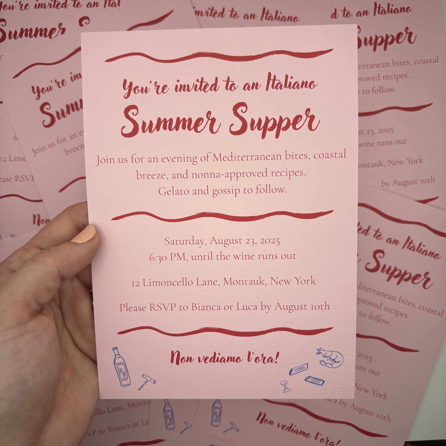 Hand holding a pink invitation card with red text and decorative elements on a matching background.