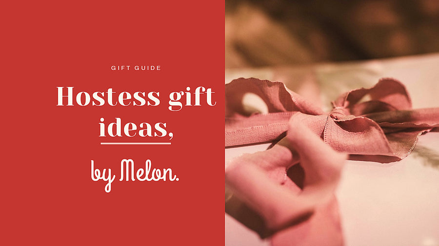 A hand tying a dusty-rose silk ribbon into a bow on a wrapped hostess gift