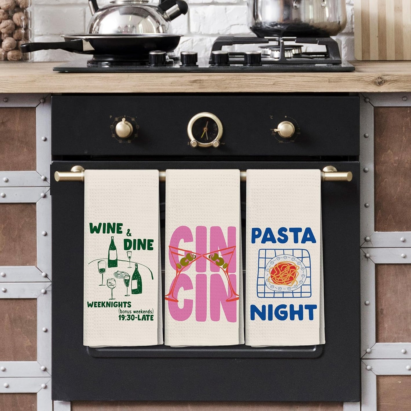 Three kitchen towels with humorous prints hanging on a black stove.