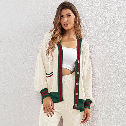 Woman wearing a white cardigan with green and red accents, white top, and beige pants against a light gray background.