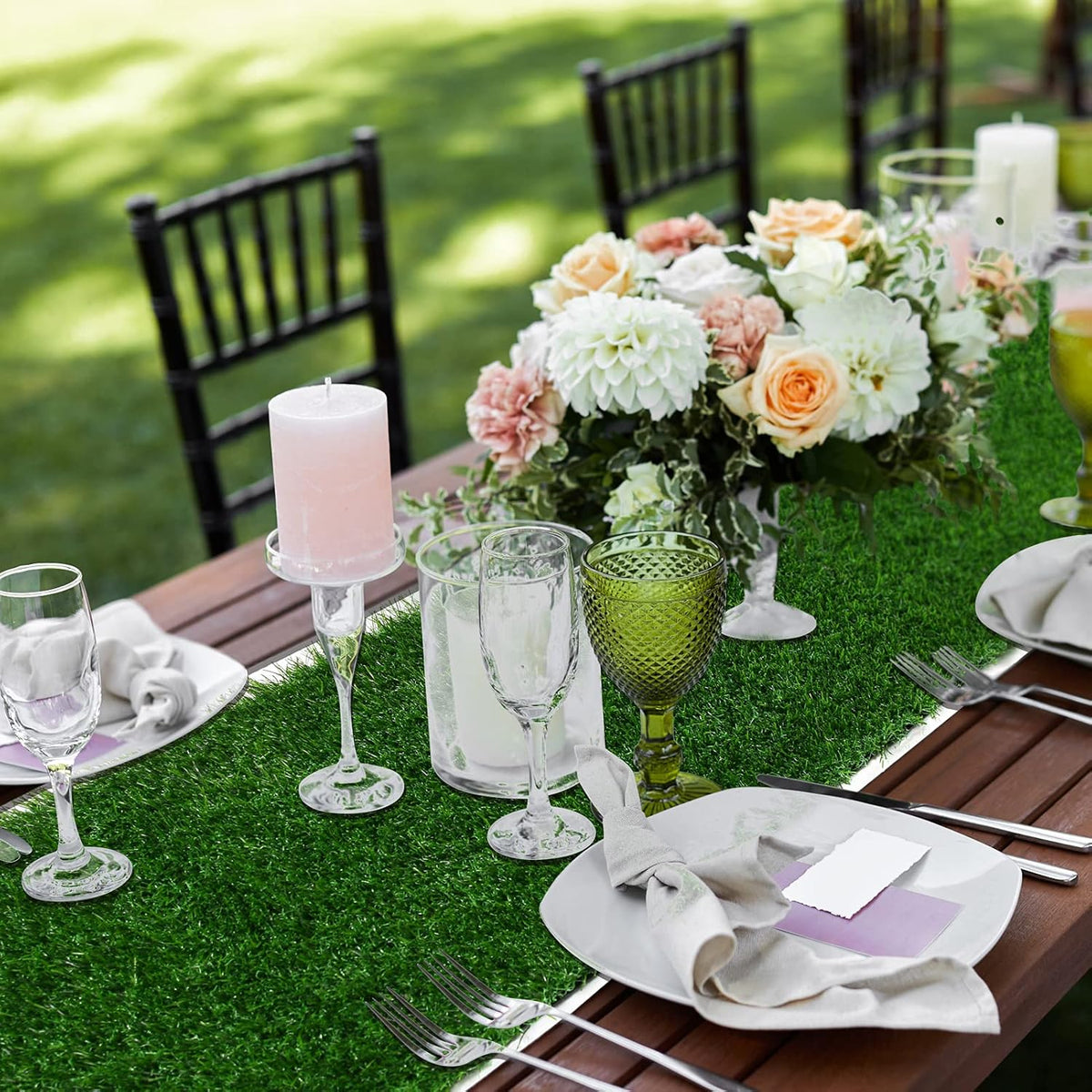 Outdoor table setting with floral centerpiece, candles, and glasses on a turf table runner
