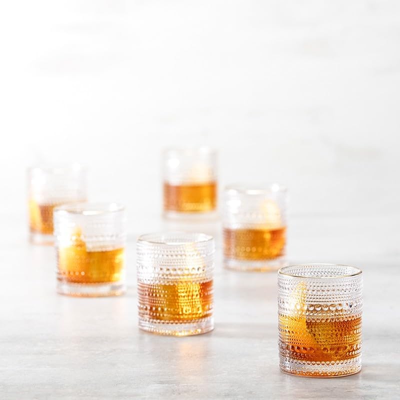 Set of textured glass tumblers filled with a amber liquid on a light background