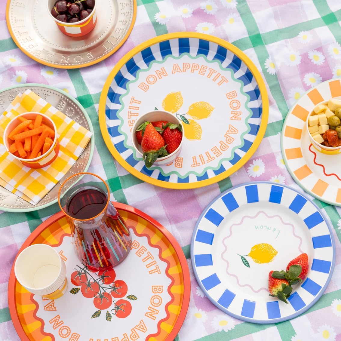 Colorful plates with 'Petit Bon Appetit' text and fruit illustrations on a patterned tablecloth.