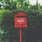 Red post mailbox surrounded by greenery — Mail by Melon quarterly party envelope subscription.