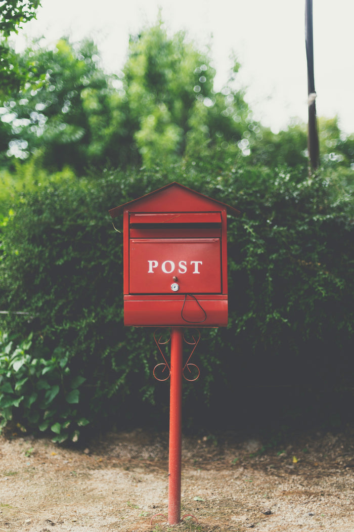 Red post mailbox surrounded by greenery — Mail by Melon quarterly party envelope subscription.