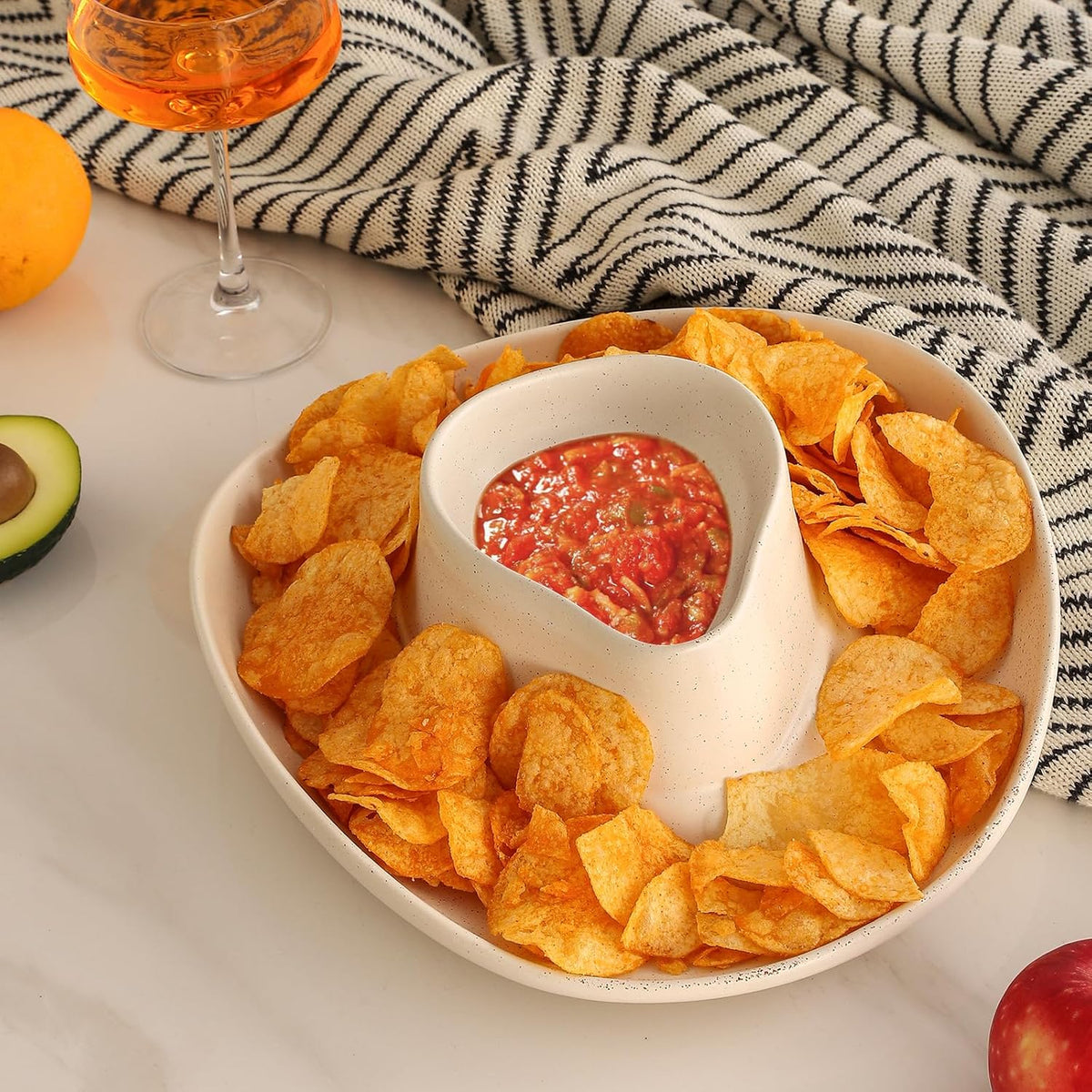 Bowl of tortilla chips with salsa on a table with a glass of orange juice and an avocado in a cowboy hat serving dish