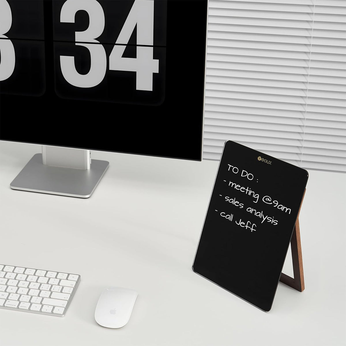 Black digital display with wooden stand on a desk next to a computer monitor and keyboard.