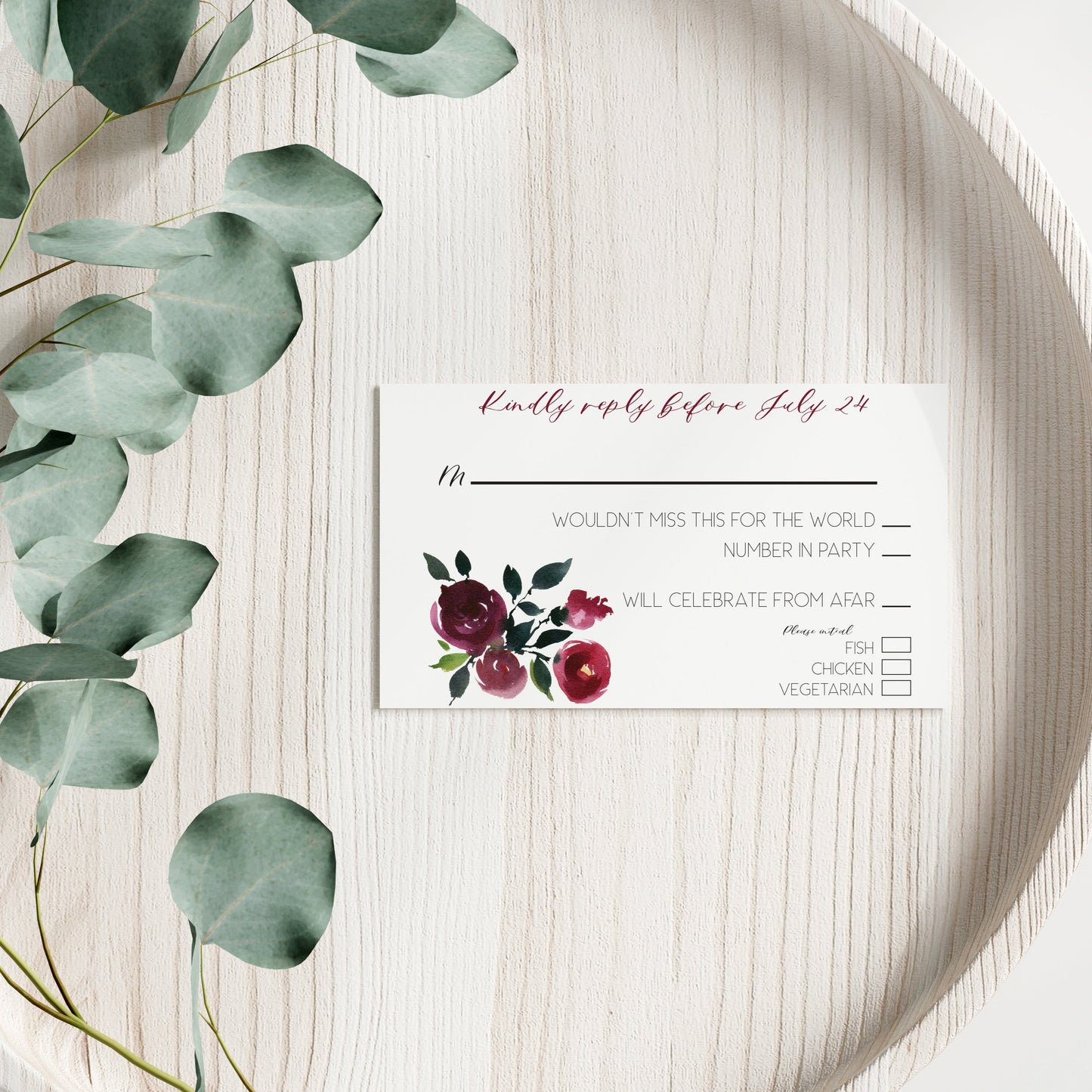 Floral RSVP card on a wooden surface with eucalyptus leaves.