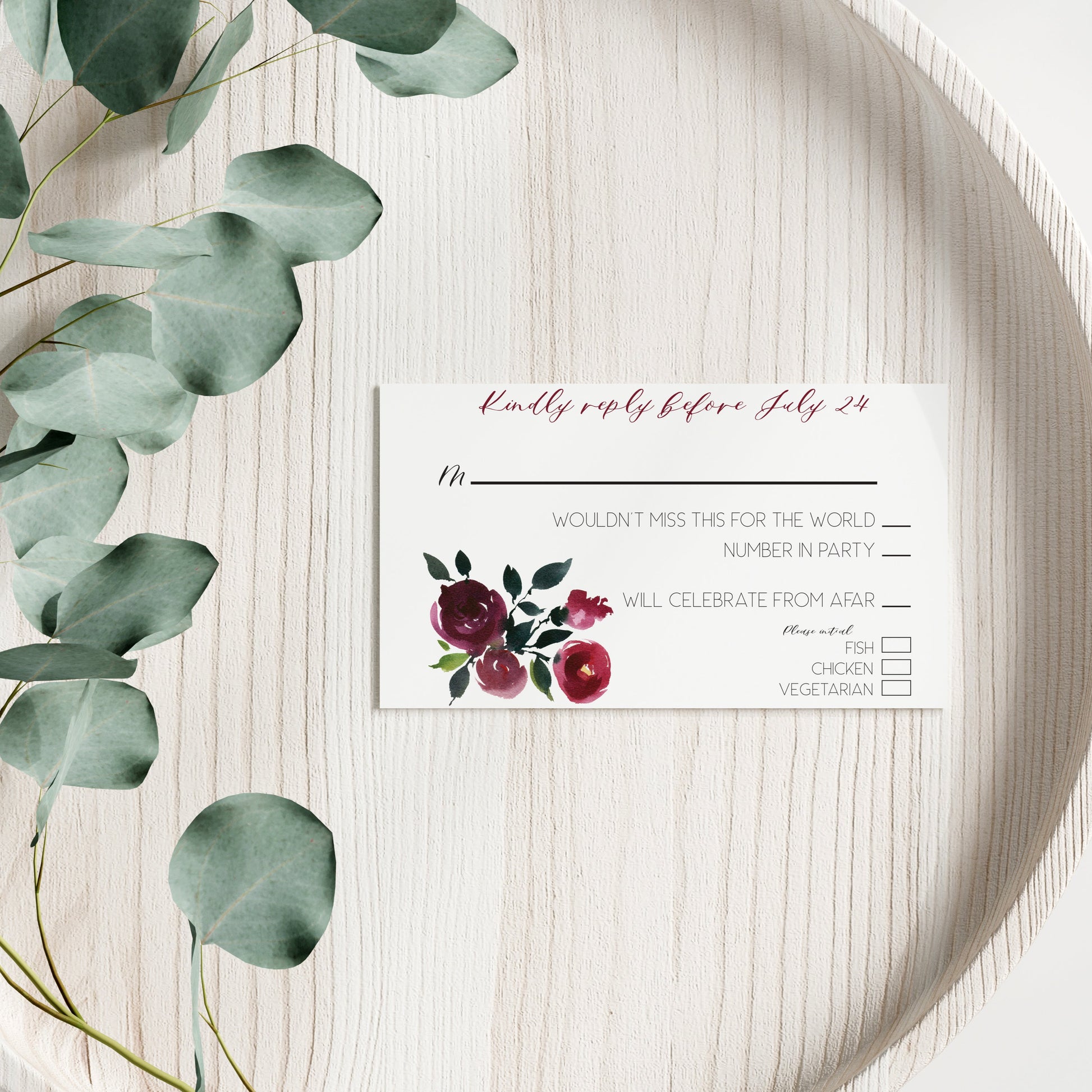 Floral RSVP card on a wooden surface with eucalyptus leaves.