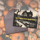 Halloween-themed card with haunted house illustration and pumpkins in the background