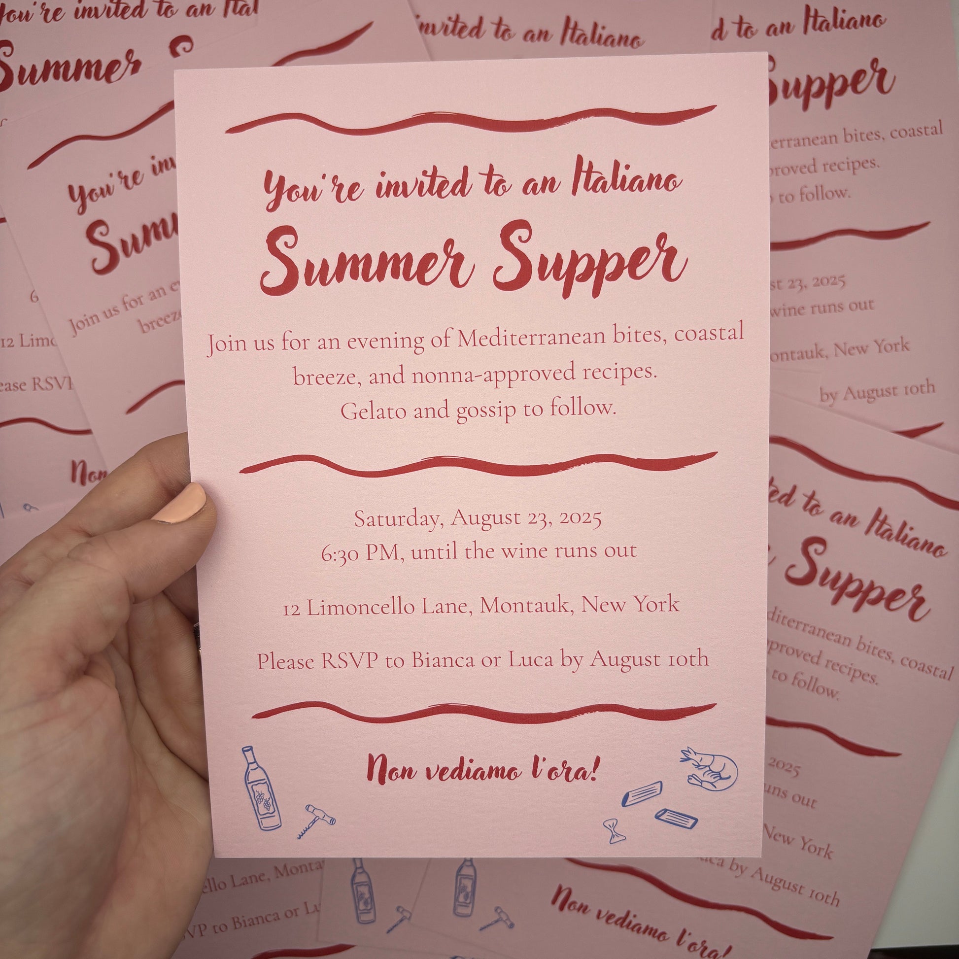 Hand holding a pink invitation card with red text and decorative elements on a matching background.